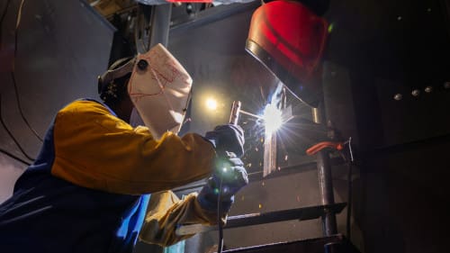 A welder welding pipes with proper safety equipment